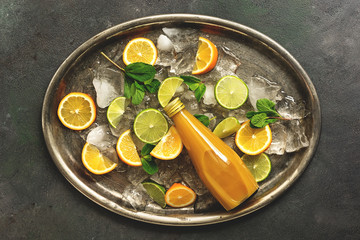 Orange juice with pulp in a bottle, slices of citrus and crushed ice on a vintage metal tray. Top view, flat lay.