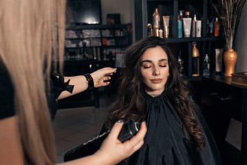 Female hairdresser makes hairstyle on young woman with brunette hair in salon.