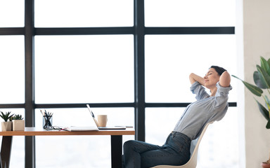 Happy european girl leaning on chair at workplace side view