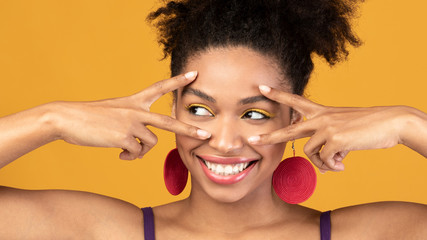 Happy afro girl showing v sign at orange studio