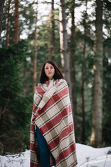 Girl with red hair in warm blanket in forest