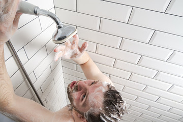 Man in soapy foam, worried about the lack of water in the shower, he looks with displeasure at the...
