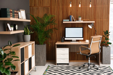 Comfortable workplace with computer near wooden wall in stylish room interior. Home office design - obrazy, fototapety, plakaty