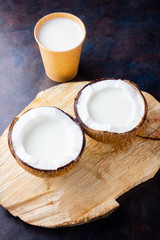 Coconut milk and coconut in paper glass on dark background. Coconut vegan milk non dairy on a wooden stand. Healthy drink concept. Alternative milk. Top view