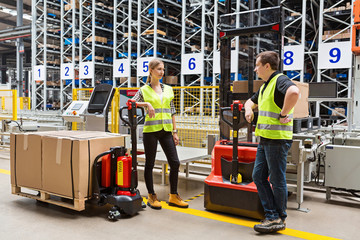 Storehouse employees in uniform standing near pallet truck and forklift in modern automatic...