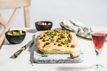 Foaccia with green and black olives, rosemary and capers. White background, hard light.