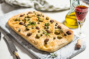 Foaccia with green and black olives, rosemary and capers. White background, hard light.