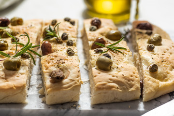 Foaccia with green and black olives, rosemary and capers. White background, hard light.