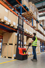 Storehouse employee in uniform working on forklift in modern automatic warehouse.Boxes are on the...