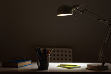 Workplace. The lamp in the dark with the light on, shines on the table