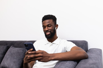 Handsome african man making a phone call via airpods while sitting on a couch in his living room