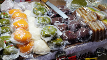 A variety of steamed rice cakes and pastries, individually wrapped in plastic wrappings, on display for sale.