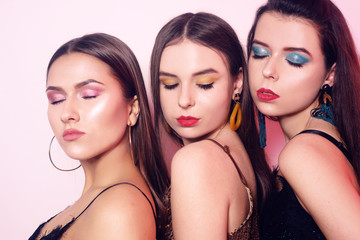 3 chic girls, portraits of models with chic bright makeup. Girls in shiny clothes, with accessories, earrings, bright makeup on a pink background. Holiday, party.
