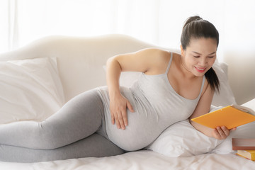 Obraz na płótnie Canvas Happy Asian pregnant are reading a book in bedroom,pregancy concept
