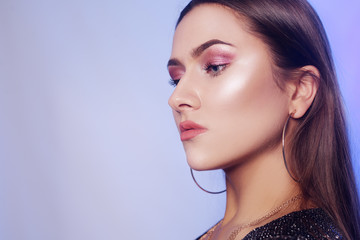Obraz premium Gorgeous brunette in a shiny black dress. Girl with long hair, chic jewelry, earrings, necklace. Delicate pink makeup. Girl on a blue