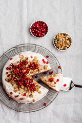 Homemade cake with cream cheese and caramel filling, topped with walnuts and pomegranate seeds on light grey linen table cloth and vintage cooling rack