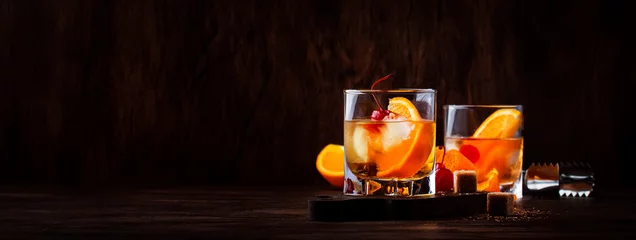 Foto op Plexiglas Alcoholische ouderwetse cocktail met sinaasappelschijfje, kers en sinaasappelschil garnituur © 5ph