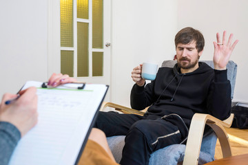 Fototapeta premium Siedzący na krześle mężczyzna u psychologa opowiada o swoich problemach. Psychologiczne leczenie uzależnień.