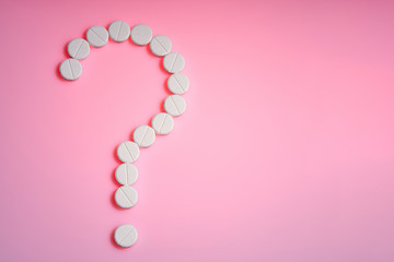 Question mark made from white pills on a pink background, flat lay with space for text.