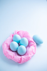 Blue Easter eggs in a pink paper nest on a blue background. Top view free space for copying. Easter concepts