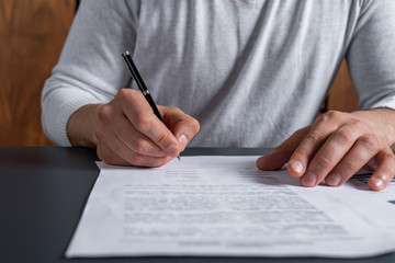Fototapeta premium A man signing the mortgage contract at the real property agent office. The concept of entering into legal power to take liabilities. Casual wearing.