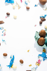 Chocolate eggs and wrapping papers sparse over a messy background, top view, easter concep