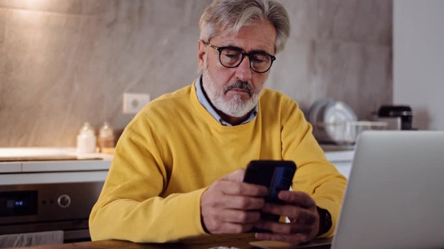 Slow motion shot of mature man using smartphone in the kitchen