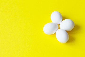 Four white eggs lie on a colorful yellow background.
