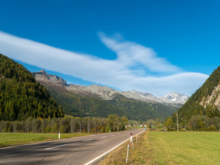 Naklejka premium Direct rural asphalt road in the Alpine mountains valley in autumn, blue sky background