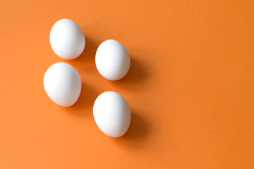 Four white eggs lie on a colorful terracotta background.