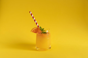Freshly squeezed orange juice with orange slices & leaves of mint. Cardboard drinking tube.Yellow background. Healthy eating concept. Prevention of coronavirus and colds with vitamin C. Copy spaсe.