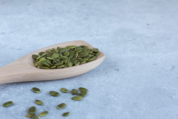 Peeled unroasted pumpkin seeds lie in a wooden spoon on a grey background.