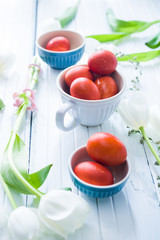 Naturally dyed eggs with red onions are inside a white bowl, with fresh tulips with white flower around, top view, easter concept, minimalistic composition