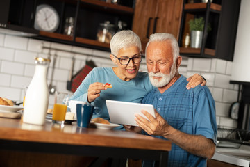 Senior couple in home kitchen looking at tablet