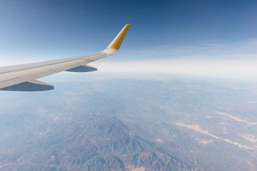 Fototapeta na wymiar ala de un avión airbus a320 sobrevolando montañas españolas, de fondo el cielo con nubes en un dia azul, soleado y claro. avión de transporte humano.