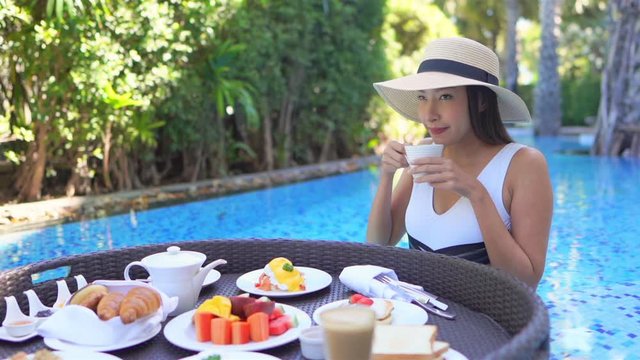 A young Asian woman in a pool chooses coffee from a floating platter of breakfast foods.
