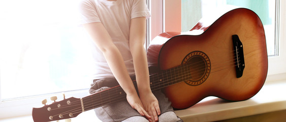 The boy is sitting on the windowsill with a guitar