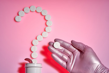 The Question mark of the pills.Question point. White pills on a pink background. In the palm of the doctor lies a white pill.
