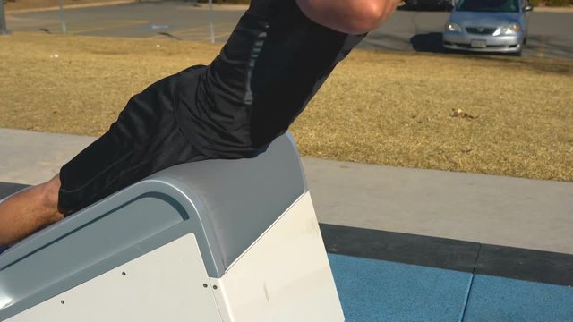 Man in black Workout Clothes does back extentions at Outdoor Park Fitness Course, medium shot profile