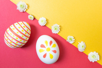 Easter concept. White eggs with marker simple children's drawings. Manual coloring. Yellow and red shades. Nearby are small white flowers. Flat lay, top view, copyspace.