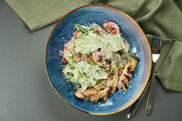 Caesar salad with croutons, parmesan, chicken, egg in blue bowl on wooden background. Restaurant serving. Top view, flat lay with copy space