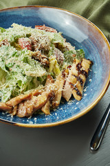 Caesar salad with croutons, parmesan, chicken, egg in blue bowl on wooden background. Restaurant serving. Close up, selective focus, vertical