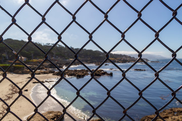 Ocean behind metal mesh fence . Restraint of liberty