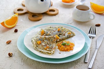 Thin crepe pancakes with poppy seeds, orange jam and chopped hazelnuts on a white plate on a light concrete background. French cuisine. Pancake day concept. Pancake Recipes.
