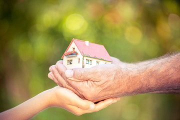 Senior man and child holding house in hands against spring green background