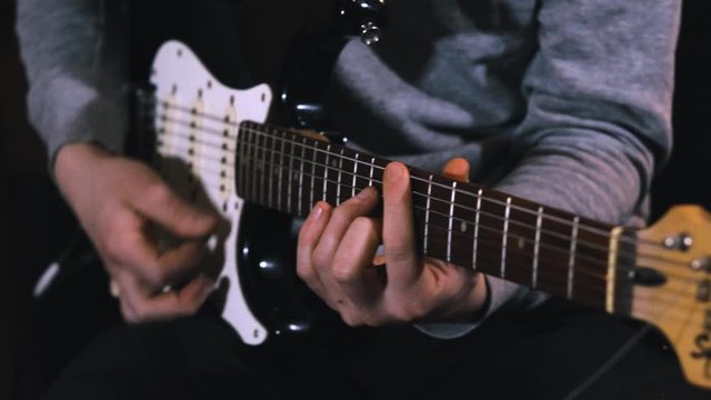 Guitarist hits the strings of the electric guitar, close up mens fingers playing music on guitar