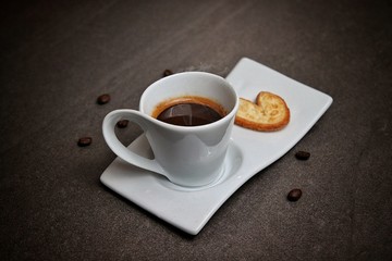 Una deliciosa taza de café caliente servido en porcelana blanca acompañado de galletas y granos de café