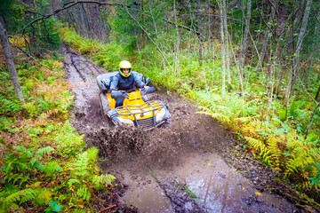 Quad bike rides through the puddles. ATV off-road top view. Spray from under the wheels. Puddles. Riding an ATV through the forest. Extreme sport. Concept - sale of ATVs. Concept - race in the forest © Grispb