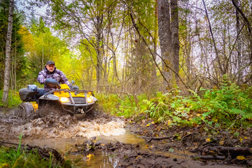 Dirt ride on an ATV. Off-road racing. A man without a helmet rides an ATV. Concept - a man is stuck. ATV stuck in the mud. From under the wheels - spray of water. Biker trying to get out of the mud.