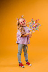 little blonde girl smiling in sunglasses holding a windmill stands on a yellow background in the Studio isolate. happy child, text space, horizontal photo